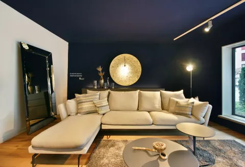 Wohnbereich mit blauer Wand, grauem Sofa, Spiegel links an der Wand und runder goldener Lampe an der blauen Wand