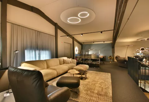 Showroom Wohnbereich mit Sofa, Sessel, Salontisch, Teppich, grosse runde Lampe an der Decke und weitere Deckenlampen
