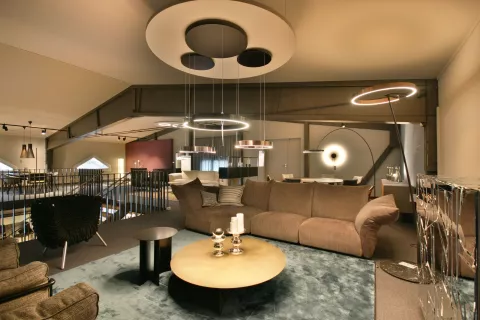 Showroom Wohnbereich mit Sofa, Sessel, Salontisch, Teppich, grosse runde Lampe an der Decke mit herunterhängenden runden Lichtern und weitere Lampen