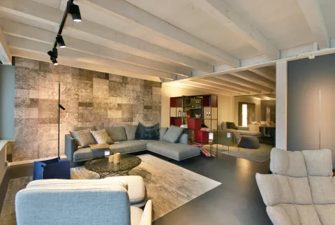 Wohnbereich mit modernem grauem Sofa, Sessel, Steinwand, verschiedene Decken- und Pendelleuchten