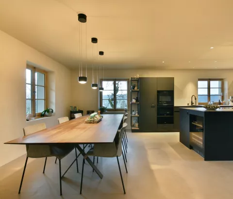 Essbereich mit moderner schwarzer Küche, drei hängenden runden Leuchten oberhalb vom Holzesstisch